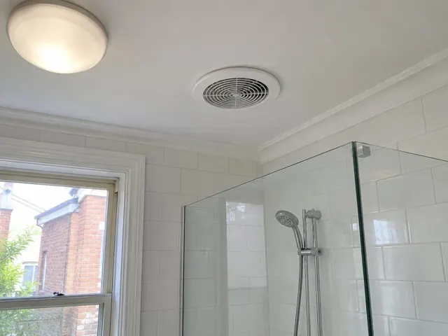 Ceiling exhaust fan above a tiled bathroom shower with glass screen and window in Double Bay